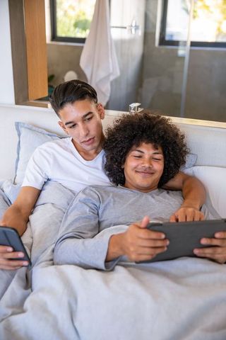 Interracial Couple Relaxing with Tablet and Smartphone in Cozy Bedroom