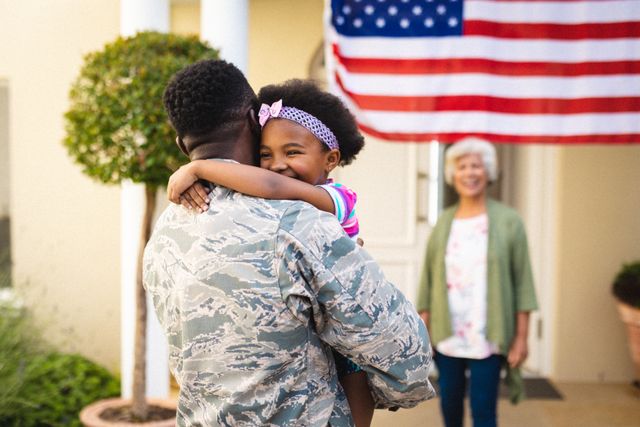 African American soldier in uniform embracing his smiling daughter at the entrance of their home with an American flag in the background. This image can be used to depict themes of family reunions, military homecomings, patriotism, and the joy of being reunited with loved ones. Ideal for use in articles, advertisements, and campaigns related to military families, homecoming events, and patriotic celebrations.