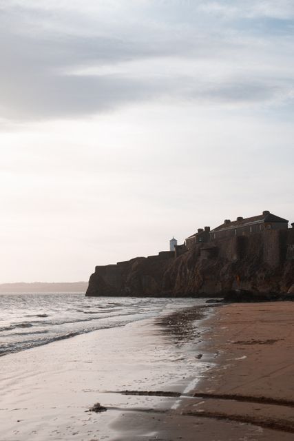 Fortress overlooking calm ocean at sunset with expansive sandy beach and waves washing ashore, creating a tranquil and serene atmosphere. Ideal for travel-related content, coastal architecture, nature relaxation themes, beach vacation promotions.