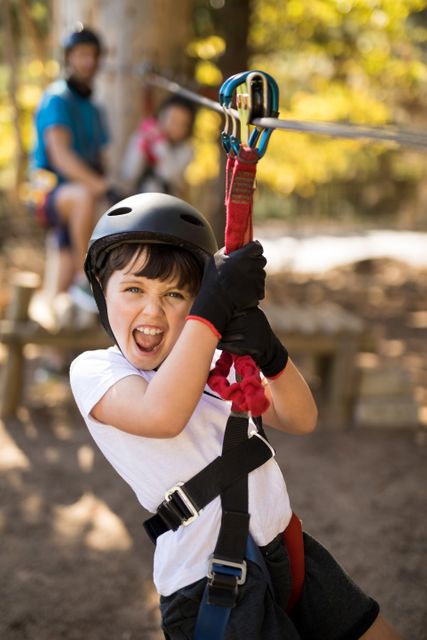 Boy having fun on a zip line in an outdoor park. He is wearing a helmet and harness for safety, smiling with excitement. Ideal for use in advertisements for outdoor adventure parks, family activities, or children's recreational programs.