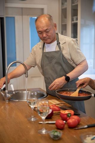 Mature man reaching for faucet while partner stirring tomato sauce on kitchen island
