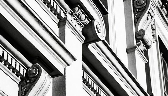 Monochrome neoclassical facade close-up showing ornate cornices, dentils, pilasters, capitals