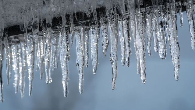 Glittering icicles hanging from roof eave dripping clear droplets against pale blue sky