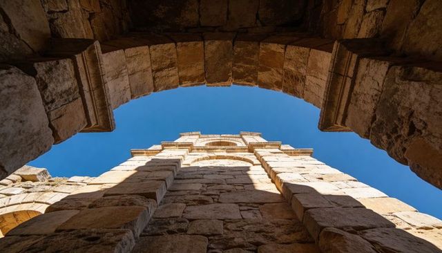 Looking up through ancient stone arch revealing weathered masonry and blue sky