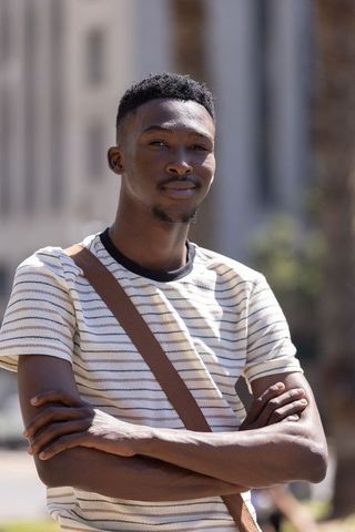 Confident african man standing with arms crossed wearing striped tee and shoulder bag
