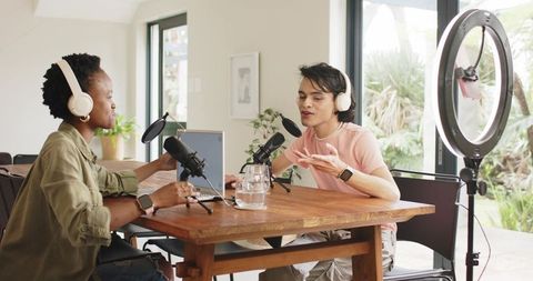 Diverse co-hosts recording podcast at home using ring light, condenser microphones and laptop