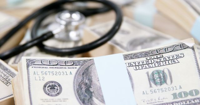 A stethoscope lies atop bundles of US dollar bills, symbolizing the intersection of healthcare and finance. It evokes discussions around medical expenses, healthcare funding, or the cost of medical services.