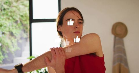 Woman stretching arm across chest during home fitness session with social thumbs-up overlays