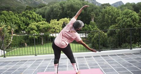 Senior woman practicing yoga outdoors on balcony with scenic view