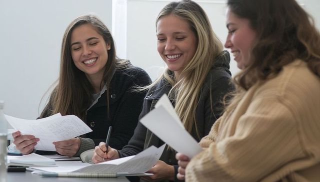 Three female students studying together, sharing notes, smiling in collaborative group work