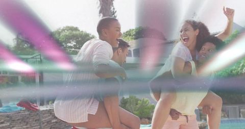 Friends laughing while giving piggyback rides at backyard pool with colorful lens flares