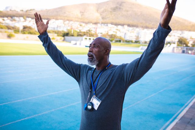 African american male coach with raised hands during training. professional runner training at sports stadium.
