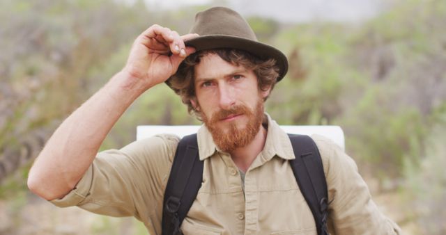 Portrait of serious bearded caucasian male survivalist trekking through wilderness, raising hat. exploration, travel and adventure, survivalist in nature.