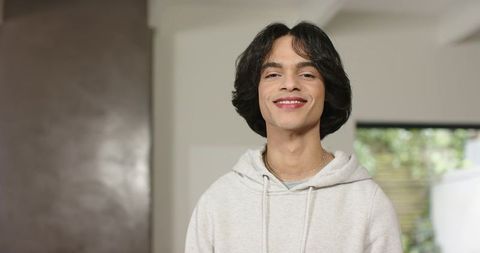 Young man smiling wearing light gray hoodie and chain necklace in modern interior portrait
