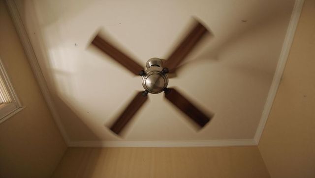 Spinning ceiling fan casting motion blur and shadows in small room with wood blades
