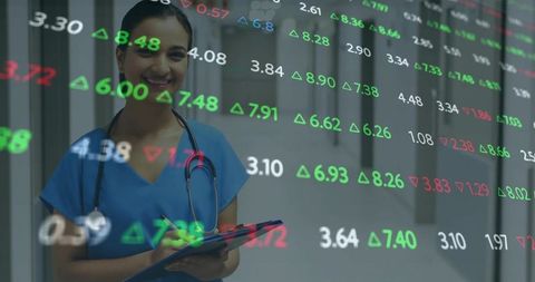 Smiling Indian nurse in blue scrubs holding tablet showing financial market data overlay