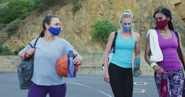 This image depicts three women wearing masks and carrying sports equipment post-practice session. Excellent for depicting group workout, promoting health and safety, and importance of friendship and exercise during a pandemic.