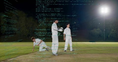 Cricket players standing on worn pitch under floodlights wearing white kit, keeper gloves