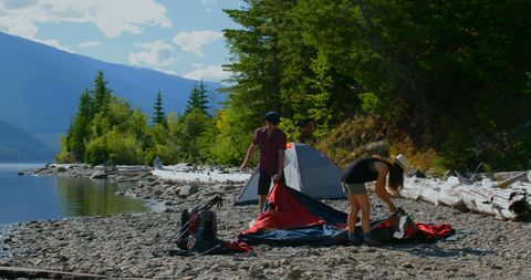 Couple setting up tent by scenic forest lake for camping