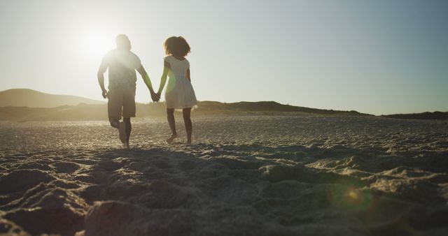 Young couple enjoys a romantic walk on the beach at sunset. Their silhouettes against the golden light create a serene outdoor setting.