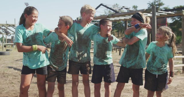 Laughing caucasian boys and girls in dirty t shirts with arms around each other on bootcamp course. Fitness, childhood, friendship, challenge and healthy lifestyle.