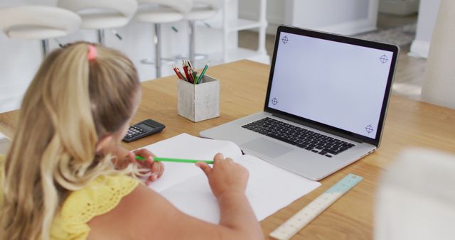 Young student focusing on online education sitting at home using laptop, notebook, and stationery. This image can be used to depict themes such as online learning, remote education, distance schooling, studying, or homework help.