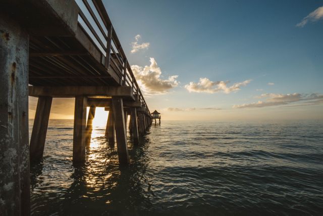 Capturing the peaceful beauty of an evening sunset by the ocean, this view under a coastal pier invites viewers to appreciate nature's serenity. Ideal for travel brochures, relaxation-themed projects, or backgrounds needing a touch of tranquility and natural beauty.