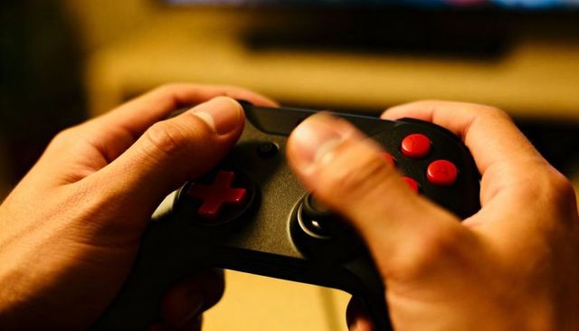 Focused gamer gripping black wireless controller with red buttons and D-pad in warm living room