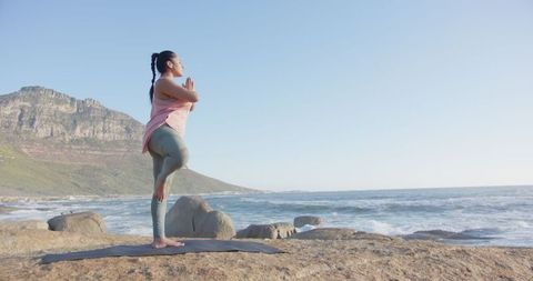 Woman Practicing Yoga Tree Pose on Rocky Ocean Shore for Balance and Serenity