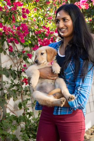 Woman holding golden retriever puppy outdoors by colorful bougainvillea