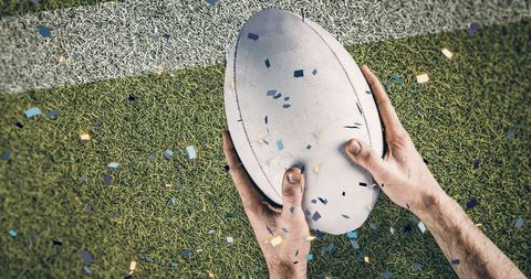 Hand Holding Rugby Ball with Confetti Celebration on Field