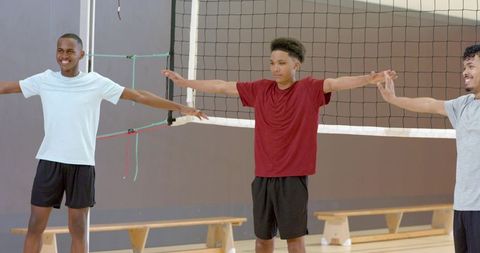 Multiracial male teammates practicing volleyball warm-up stretch on indoor court