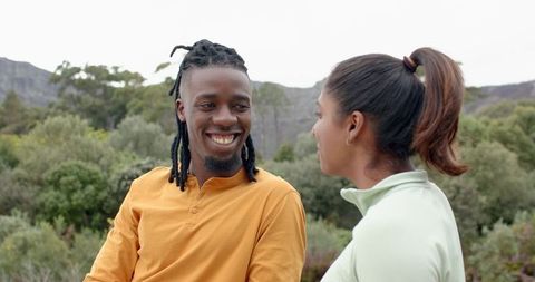 Diverse couple smiling and talking during nature outing, dreadlocked man in mustard henley