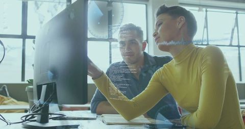 Tech lead pointing at monitor guiding coworker through code review in modern workspace