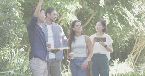 Multicultural team walking and brainstorming in sunlit garden with tablet and clipboard
