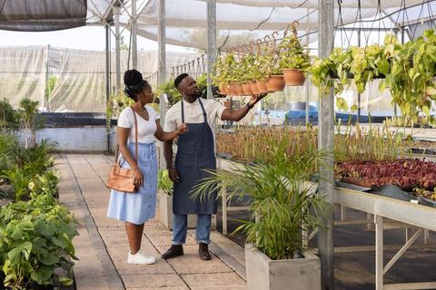 Nursery worker guiding shopper in greenhouse while inspecting hanging terracotta pot plants