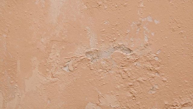 Peeling peach plaster wall showing flaking paint, cracked textured stucco surface