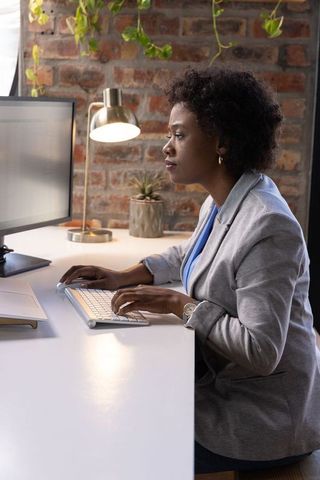 Professional woman typing at modern office desk with greenery