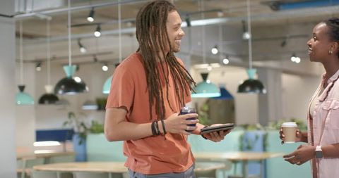African American coworkers chatting in modern open-plan lounge holding tablet and coffee