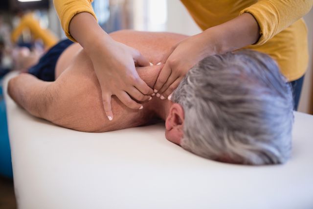 Senior man lying on bed receiving neck massage from female therapist. Ideal for use in healthcare, physical therapy, and wellness contexts. Suitable for illustrating elderly care, rehabilitation, and therapeutic treatments.