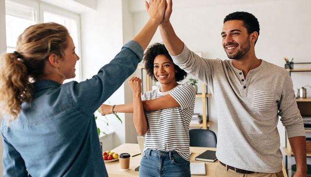 High-fiving coworkers celebrating project win in bright collaborative office workspace