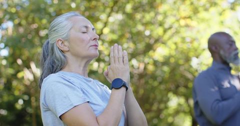 Mature couple practicing outdoor meditation wearing smartwatch in sunlit garden for wellness
