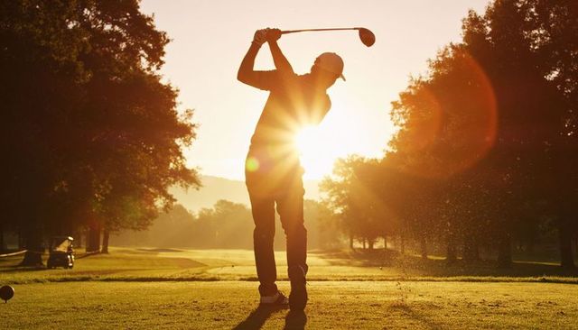 Silhouetted golfer swinging driver at sunrise on fairway with golden hour lens flare