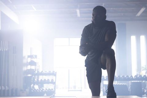 African american man stepping onto plyo box training explosively in backlit industrial gym