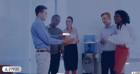 Business team collaborating around tablet by water cooler presenting ideas in bright office
