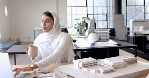Architect in hijab working on model while having coffee in office