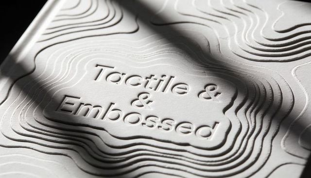 Embossed paper topography with tactile typography and dramatic hard-light shadows