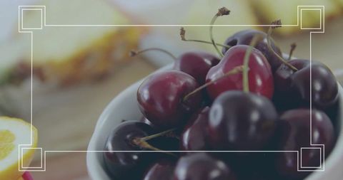 Close-up ceramic bowl of ripe cherries with lemon wedge and soft bokeh corner frame