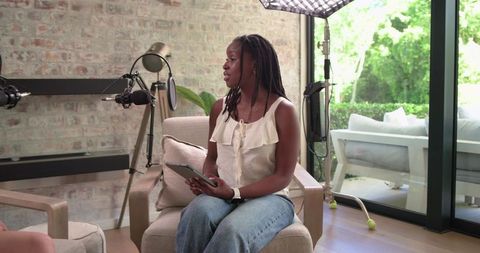 African American woman hosting podcast and interview at home studio, holding tablet