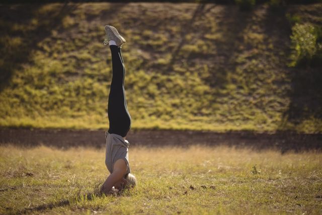 Woman practicing headstand on grassy field during outdoor boot camp. Ideal for fitness blogs, yoga tutorials, exercise programs, and healthy lifestyle promotions.
